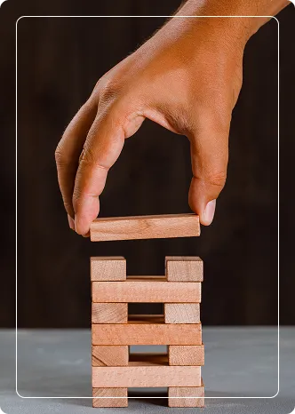 Mão ajustando blocos de madeira empilhados em torre, representando a estruturação segura e análise de viabilidade financeira de projetos.