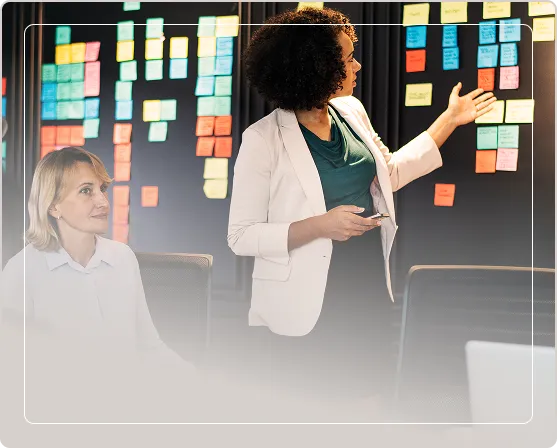 Duas profissionais em reunião de reestruturação de empresas analisando um quadro com post-its coloridos para reengenharia de processos na CIS Consultoria.